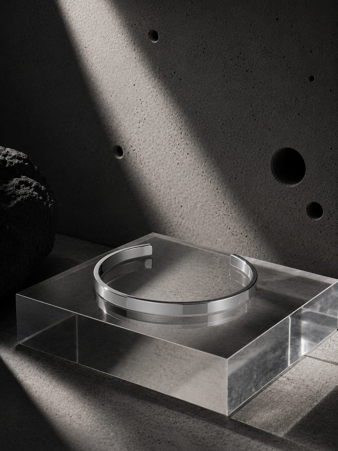 Silver bracelet on a reflective surface with a concrete wall background
