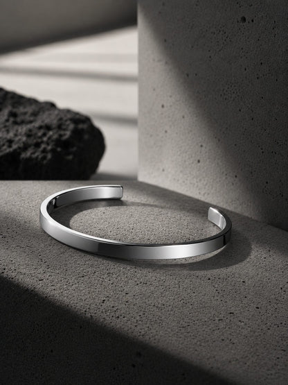 Silver bracelet on a concrete surface with a concrete pillar and dark rock in the background