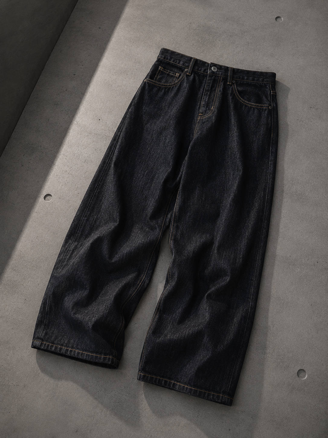 Black straight-leg denim jeans laid flat on a concrete floor.
