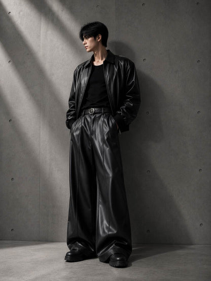 Person wearing a black leather outfit against a gray concrete wall.
