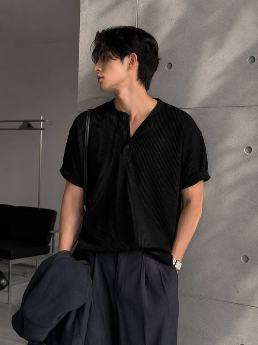 Person wearing a black shirt and dark pants against a gray wall.